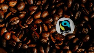 Viele geröstete Kaffeebohnen, im rechten Bilddrittel das schwarz-blau-gelbe Fairtrade-Siegel