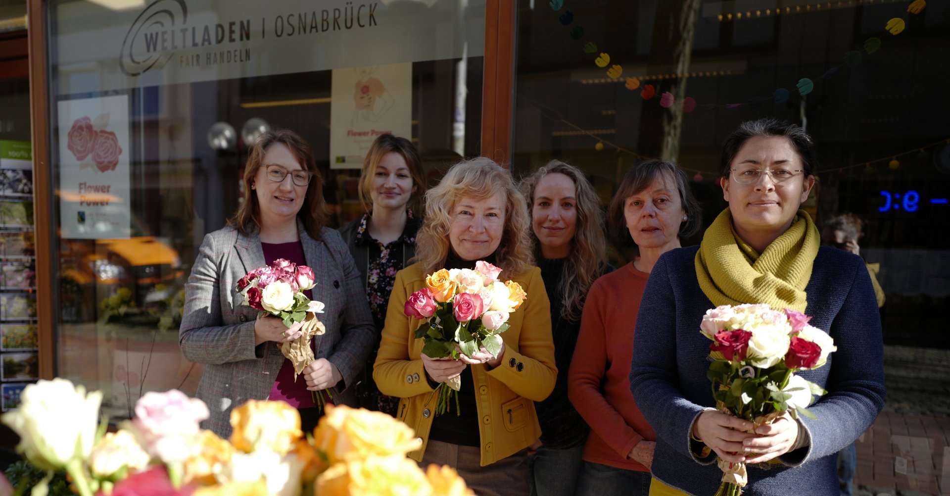 6 Frauen mit Blumensträußen in den Händen, im Vordergrund ein gelber Rosenstrauß